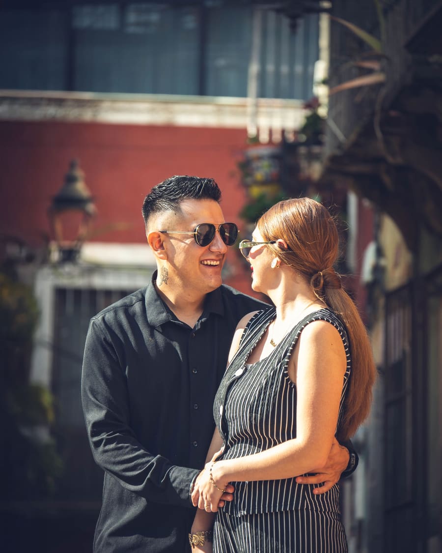A mature woman smiling outdoors with an attentive companion.